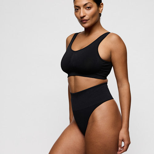 Primadonna NUDDA shapewear thong in black worn by a model showcasing its smooth high-waisted design.